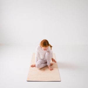 child sitting on orange pilates mat with head down
