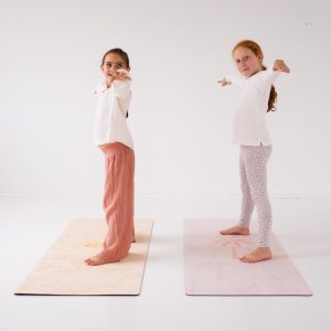two children standing sideways on pilates mats with arms out