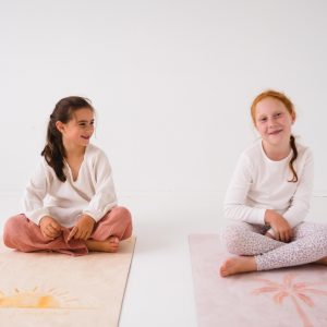 two children sitting on pilates mats smiling