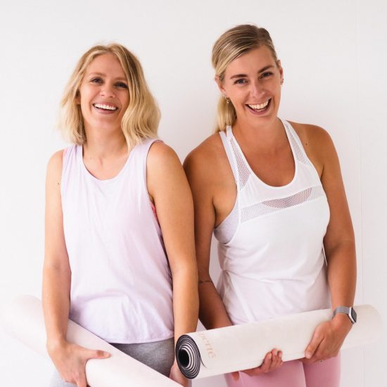 two women holding rolled up pilates mats smiling